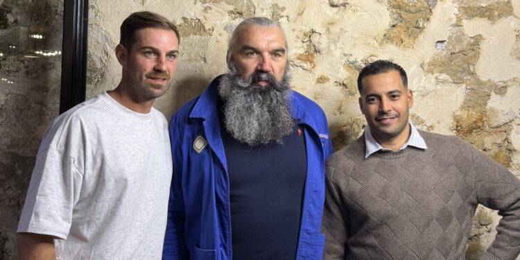 Une salle de restaurant chaleureuse et conviviale, grandes tables en bois prêtes pour un repas de partage, planches de viandes grillées et burgers généreux posés au centre, ambiance décontractée.
