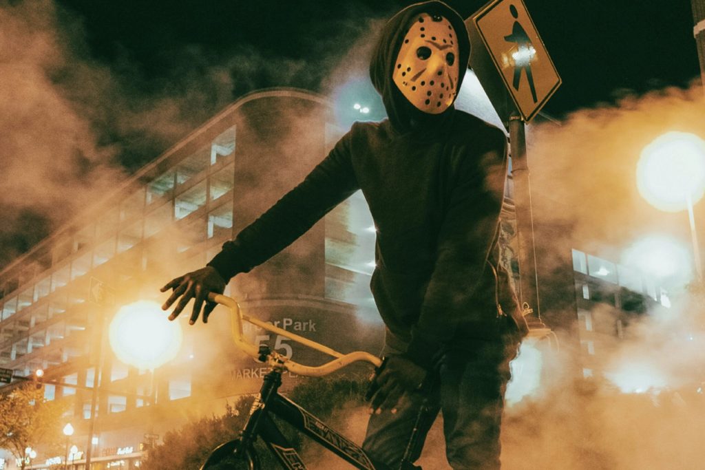 Une petite troupe de cyclistes déguisés pour Halloween roule de nuit à vélo électrique dans les rues éclairées d'une ville, ambiance festive et légèrement mystérieuse.